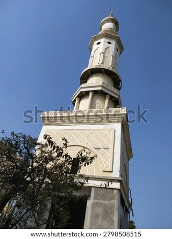 Low-angle view of a mosque minaret featuring elegant Islamic architecture against a clear blue sky. The tower showcases intricate geometric details and a harmonious cream-and-white color palette, symbolizing spirituality, culture, and architectural beauty. Ideal for themes related to religion, worship, Islamic heritage, travel, and cultural landmarks.