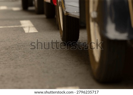Low-angle view of multiple car wheels lined up on an asphalt parking area with painted white parking markers. Visible tire treads and wheel rims in soft