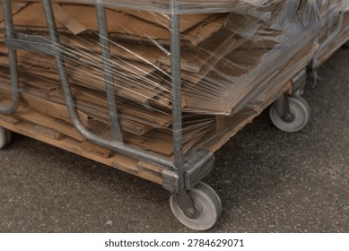 Lowangle view of multiple wrapped carts on asphalt, repetitive metal frames and casters form pattern, cloudy sky above and warehouse facade beyond, pragmatic