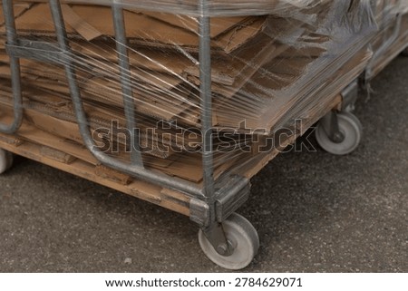Lowangle view of multiple wrapped carts on asphalt, repetitive metal frames and casters form pattern, cloudy sky above and warehouse facade beyond, pragmatic