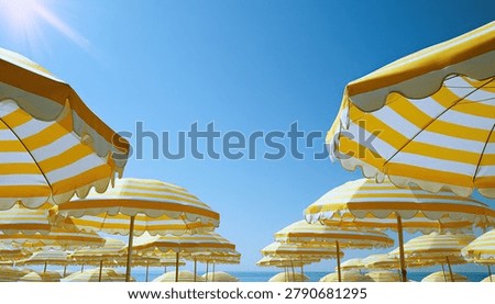 A low-angle view of numerous beach umbrellas with yellow and white stripes, set against a vibrant blue sky with the sun shining.