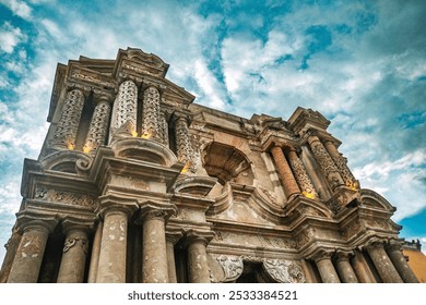 A low-angle view of an ornate historical building facade with intricate carvings against a cloudy blue sky in Antigua, Guatemala. - Powered by Shutterstock