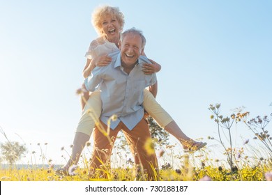 Low-angle view portrait of a happy senior man laughing while carrying his partner on his back, in a sunny day of summer in the countryside - Powered by Shutterstock