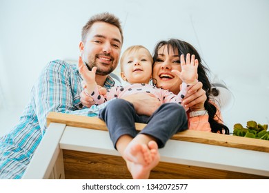 A Low-angle View Portrait Of Young Happy Family With A Barefoot Toddler Girl Sitting At Kitchen Table, Saying 