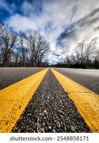 A low-angle view of a road with two solid yellow lines running down the center.