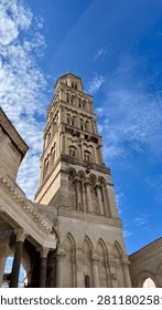 Low-angle view of the Romanesque bell tower of the Cathedral of Saint Domnius rising above Diocletian's Palace under a blue sky with wispy clouds in Split, Croatia.