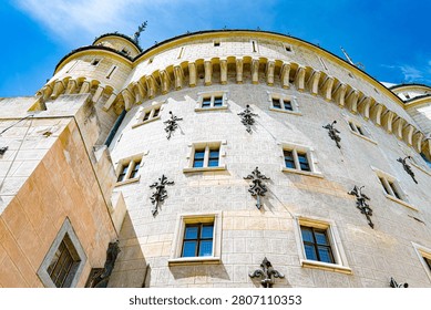 Low-angle view of a round neo-Gothic tower of Bojnice Castle showing pale stone walls, arched windows, decorative ironwork and a crenellated cornice under a clear blue sky.