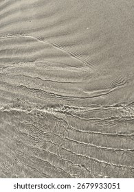 Low-angle view of shallow wavelets creating bright ripple lines over wet beach sand under soft sunlight.
