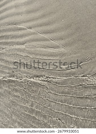 Low-angle view of shallow wavelets creating bright ripple lines over wet beach sand under soft sunlight.