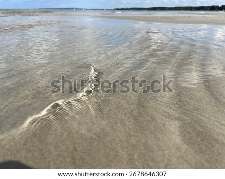 Low-angle view of shallow wavelets forming bright ripples on wet beach sand under soft sunlight.