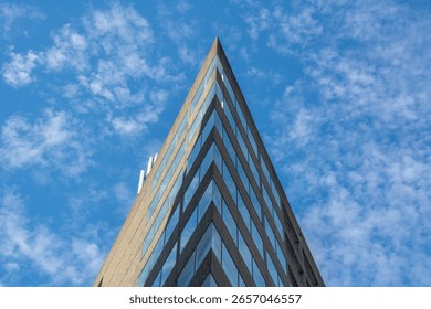 Low-angle view of a sharp-edged modern office building in Nashville, Tennessee, with reflective glass windows and concrete facade set against a bright blue sky with scattered clouds