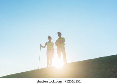 Low-angle view of the silhouette of a man pointing to the horizon while standing next to his female partner, on a professional golf course against sunshine and clear blue sky - Powered by Shutterstock