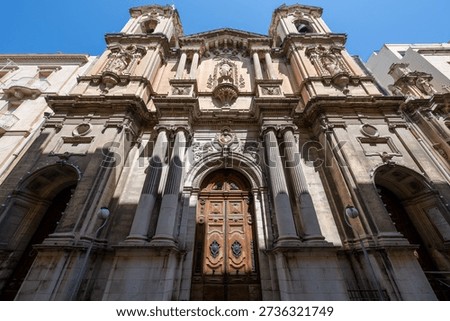 Low-angle view of St. Paul's Shipwreck Church in Valletta, showing the Baroque stone facade, twin bell towers, and carved wooden entrance door in bright summer light.