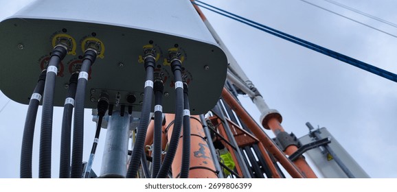 Low-angle view of a telecom antenna with multiple coax cables and hardware on a mast against cloudy sky, wireless infrastructure.