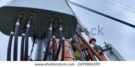Low-angle view of a telecom antenna with multiple coax cables and hardware on a mast against cloudy sky, wireless infrastructure.