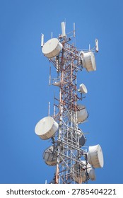Low-angle view of a telecommunication tower with multiple cellular antennas and dish equipment mounted on a steel lattice structure against a clear blue sky.