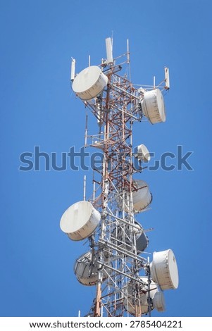 Low-angle view of a telecommunication tower with multiple cellular antennas and dish equipment mounted on a steel lattice structure against a clear blue sky.