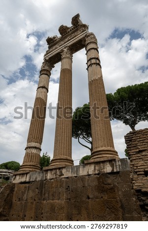Low-angle view of three fluted Corinthian columns and entablature ruins of the Temple of Venus Genetrix in the Roman Forum, under cloudy sky.