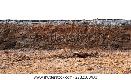 A low-angle view through the mound to the cross-section of the soil layer beneath an asphalt road that has been dug with a barkhoe in preparation for the construction of a road renovation project.