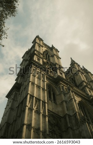 Low-angle view of the towering Gothic architecture of Westminster Abbey in London, featuring intricate stone details and clockface against a soft cloudy sky.