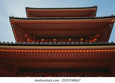 Low-angle view of a traditional Asian pagoda with intricate roof patterns, showcasing architectural beauty against a clear sky. - Powered by Shutterstock