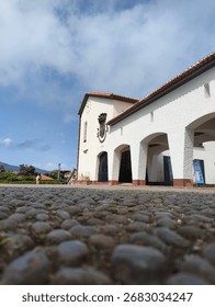 Low-angle view of a traditional whitewashed building with cobblestone foreground in Madeira, Portugal, under a blue sky with scattered clouds.