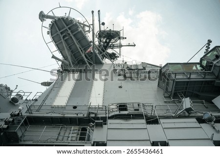 Low-angle view of the USS Intrepid's command tower featuring satellite dishes, antennas, and viewing platforms. The steel structure reflects the carrier s role in naval communication and observation.