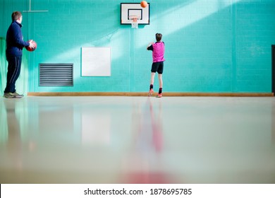 Low-angle Wide Shot Of A Coach Watching A High School Student Play Basketball During A Gym Class.