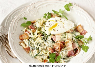 Low-Carb Keto Carbonara Pasta With Spaghetti (noodles) Of Zucchini With Cream, Fried Bacon And Poached Egg. Decorated With Pea Sprouts. In A Beautiful Light Dish. Recipes For Fatty Protein Foods 