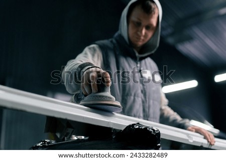 lower angle of an auto mechanic at a service station polishing the front of a white car