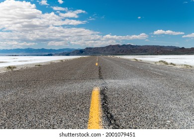 Lower Angle Of An Empty Road With Some Mountains On The Horizon Surrounded By Salt Flat Land. Bonneville Salt Flats, Utah