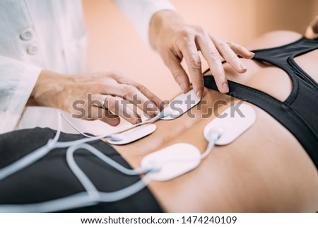 Lower Back Physical Therapy with TENS Electrode Pads, Transcutaneous Electrical Nerve Stimulation. Therapist Positioning Electrodes onto Patient's Lower Back