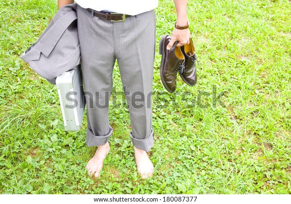 Lower\
body of businessman standing on the grass\
barefoot