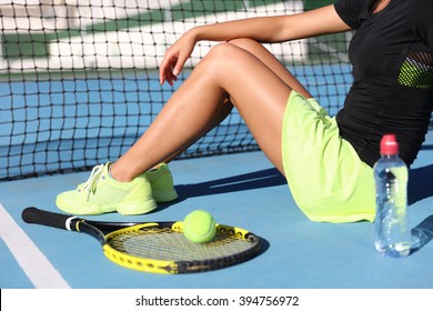 Lower body closeup of tennis player woman resting sitting on outdoor court showing tennis racket / racquet, ball and water bottle wearing yellow sportswear outfit. Sports shoes and skirt. - Powered by Shutterstock