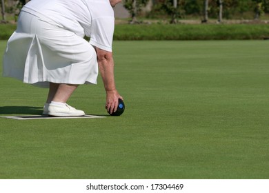 Lower Body Of An Elderly Female Wearing White Clothing And Holding A Lawn Bowling Ball About To Bowl.