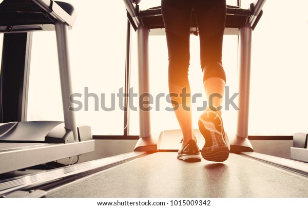 Lower body at legs part of Fitness girl running on\
running machine or treadmill in fitness gym with sun ray. Warm\
tone. Healthy and Exercise activity concept. Workout and  Strength\
training theme.