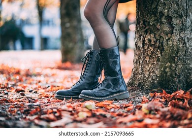 The Lower Body Of A Stylish Woman Wearing Black Combat Boots With Rose Prints Leaning On A Tree In Colorful Leaves