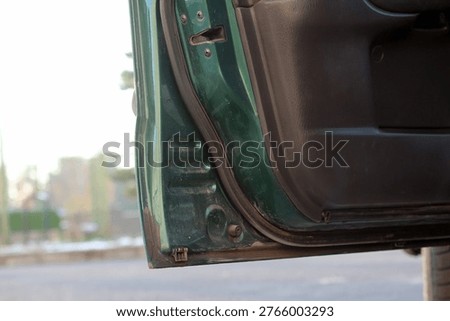 The lower corner of the open front door of a dark green Mazda 626, showing the door seal, hinge, and interior trim.