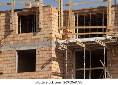 lower facade showing scaffold platforms and open bays, stacked blockwork, metal props and safety railings, gritty textures, closeup perspective suggesting trade work and material staging at ground