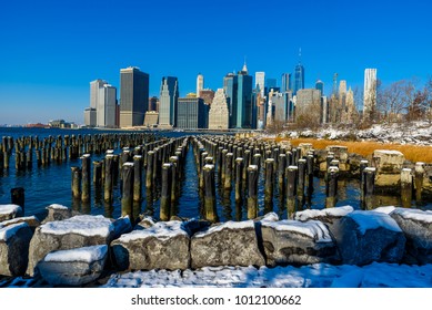 Lower Manhattan Skyline Panorama In Snowy Winter Time From Brooklyn Bridge Park Riverbank, New York City, USA