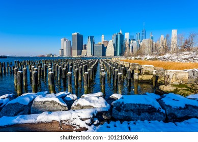 Lower Manhattan Skyline Panorama In Snowy Winter Time From Brooklyn Bridge Park Riverbank, New York City, USA