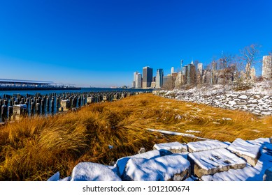 Lower Manhattan Skyline Panorama In Snowy Winter Time From Brooklyn Bridge Park Riverbank, New York City, USA