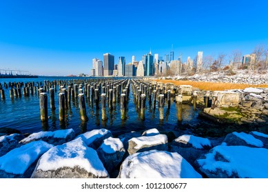 Lower Manhattan Skyline Panorama In Snowy Winter Time From Brooklyn Bridge Park Riverbank, New York City, USA