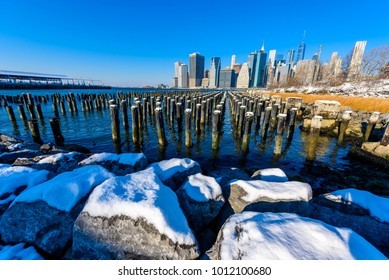 Lower Manhattan Skyline Panorama In Snowy Winter Time From Brooklyn Bridge Park Riverbank, New York City, USA