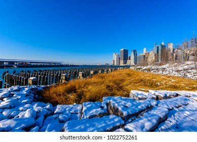 Lower Manhattan Skyline Panorama In Snowy Winter Time From Brooklyn Bridge Park Riverbank, New York City, USA