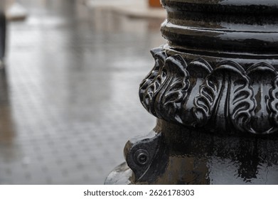 The lower part of a lamppost with a pattern on a wet rainy street. Background for describing bad weather, sad mood.