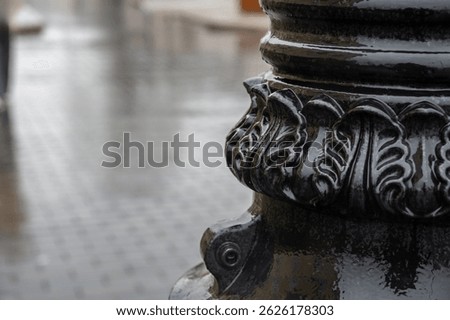 The lower part of a lamppost with a pattern on a wet rainy street. Background for describing bad weather, sad mood.