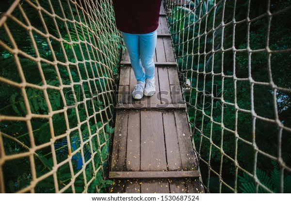 lower section of a girl standing on a swinging\
bridge in the rainforest