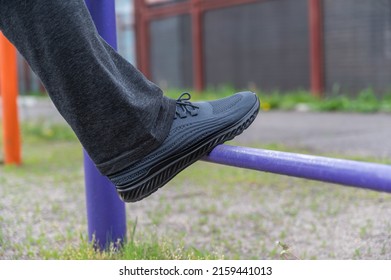 The Lower Section Of A Mature Man Exercising On An Outdoor Sports Field. Legs Of A Man Straining On Athletic Trainers. Gymnastic Exercises.