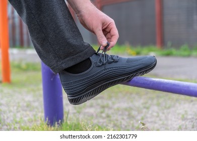 The Lower Section Of A Mature Man Exercising On An Outdoor Sports Field. Legs Of A Man Straining On Athletic Trainers. Gymnastic Exercises.